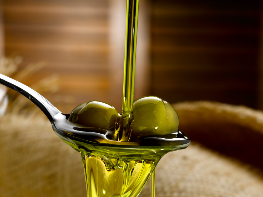 Olive oil in a stream pouring onto spoon holding a couple of olives